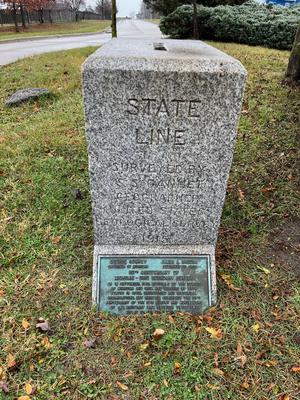 A granite block with the inscription 'STATE LINE
SURVEYED BY
S. S. GANNET
GEOGRAPHER
UNITED STATES
GEOLOGICAL SURVEY
1915' a plaque below the inscription commemorates the 50th anniversary of the boundary survey