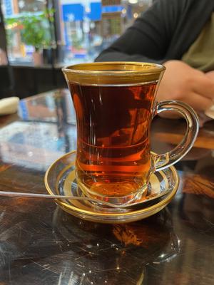 a glasss teacup in a glass saucer, both with gold stripes. The tea inside is a pleasant dark amber color.